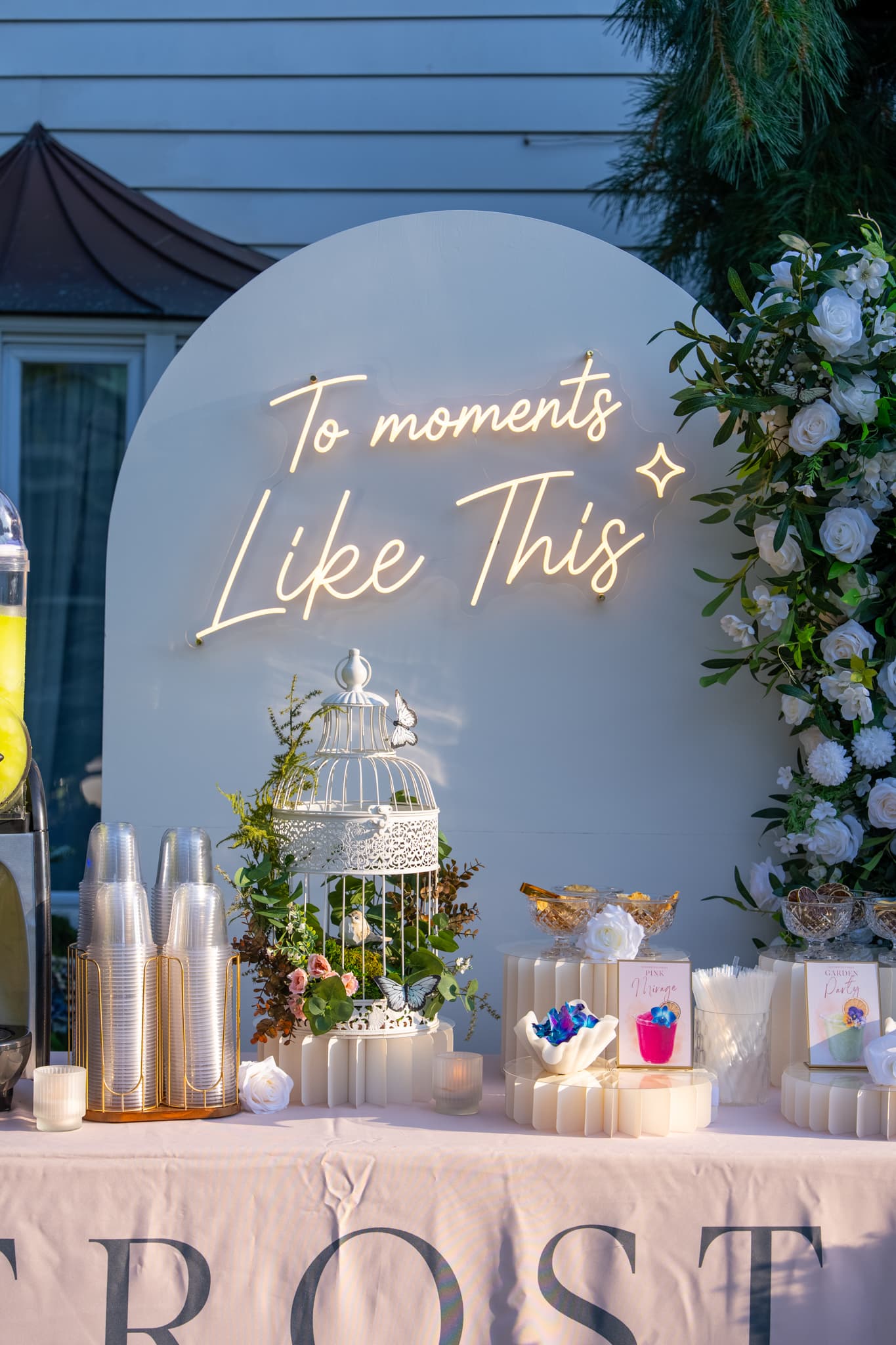 Table detail: printed flavor cards, birdcage centerpiece, and cups against the lit neon arch