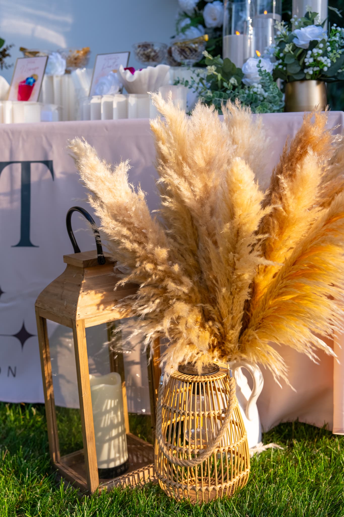 Pampas grass in a woven vase beside a lantern at the table's edge, catching golden-hour light